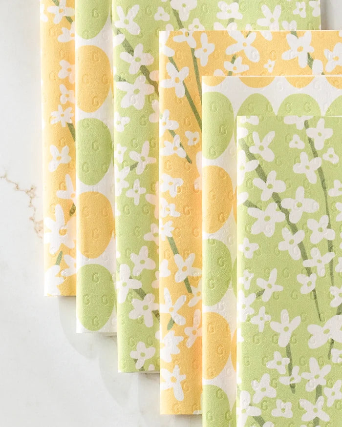 Kayla Ann’s Spring Bounty set features five folded reusable paper towels with a yellow and green floral pattern, arranged in a fan shape on a light marble surface.