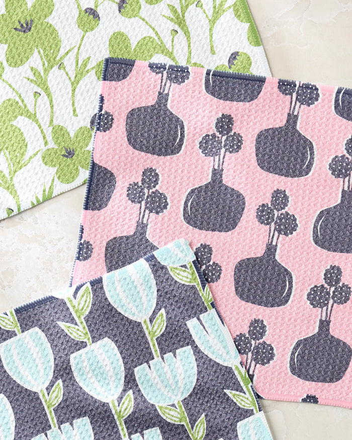 Lizzie Clark’s Spring Bouquet set features three patterned dishcloths: one with green flowers, one with blue tulips and green stems, and one with gray vases and round flowers on a pink background. All are made from recycled materials.