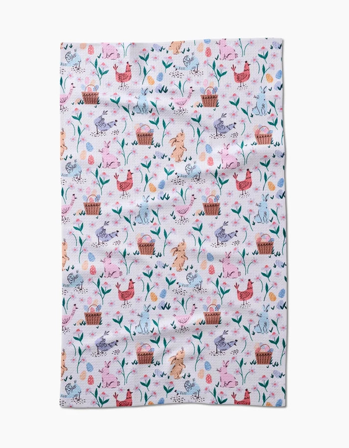 The Spring Bunnies tea towel by Charlie Rowan Designs features a colorful pastel pattern of chickens, eggs, flowers, leaves, and baskets on white. Made from ultra-absorbent recycled materials for style and sustainability.