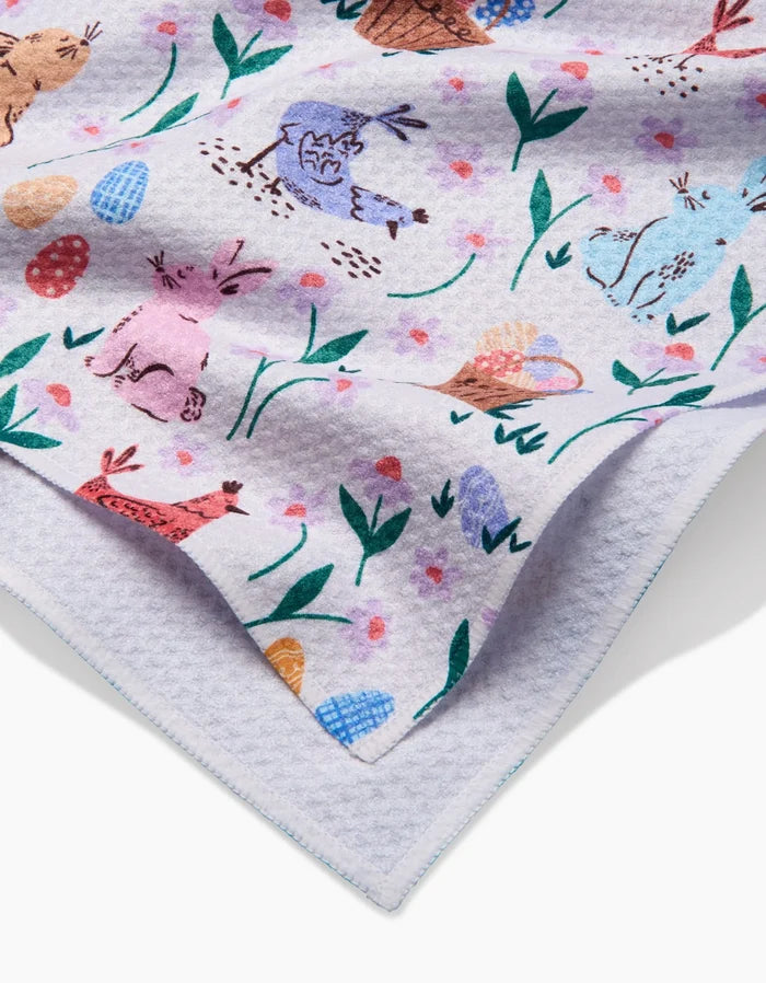 A close-up of the Spring Bunnies tea towel by Charlie Rowan Designs, made from ultra-absorbent fabric with colorful bunnies, flowers, and Easter eggs on a white background and finished with a scalloped edge.