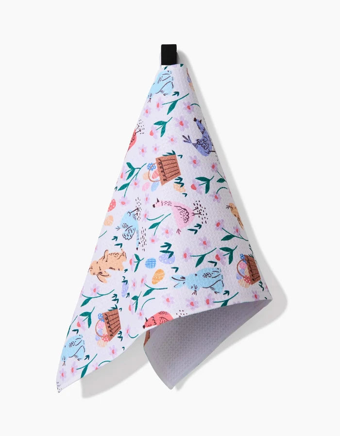The Spring Bunnies bar towel by Charlie Rowan Designs features a playful pastel pattern of flowers, cats, and yarn balls. This ultra-absorbent towel hangs from a black loop against a plain white background.