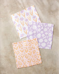 The Kayla Ann Spring Flowers set features three square, super-absorbent dishcloths in lavender, peach, and white, each with a unique floral pattern, beautifully displayed on a beige marble surface.