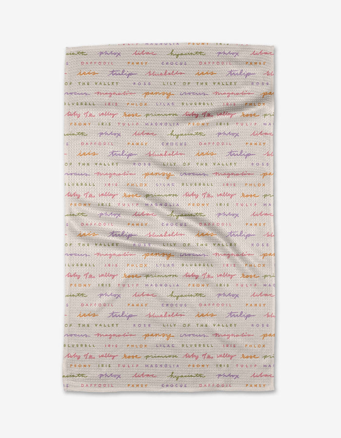The Spring Flowers by Kayla Ann is a white Geoweave cloth with colorful, cursive names of flowers—daffodil, crocus, lily of the valley, and snowdrop—repeated in horizontal lines.