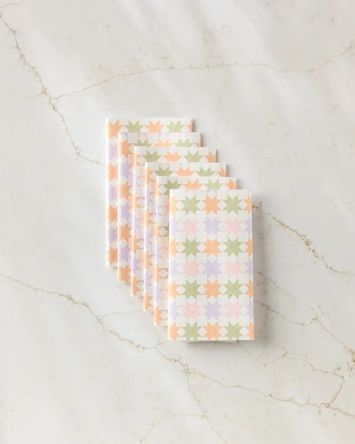Six neatly stacked Kayla Ann Spring Quilt kitchen towels, featuring an eco-friendly pastel geometric star pattern in peach, green, and lilac, are displayed on a marble surface with light brown veining.