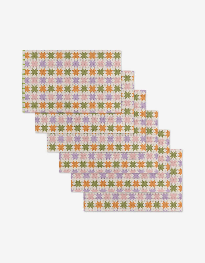 Six Kayla Ann Spring Quilt placemats, arranged in a staggered stack, display colorful stylized flowers on a light background. Made from eco-friendly post-consumer recycled materials for sustainable style.