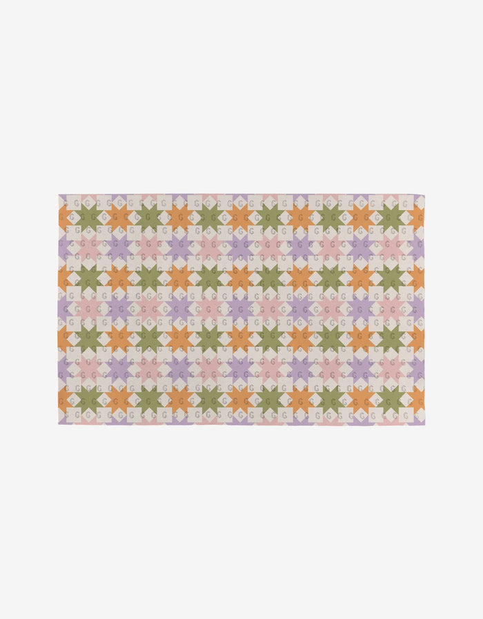 The Kayla Ann Spring Quilt features interlocking star and diamond shapes in pastel green, pink, orange, and lavender on a light background. Crafted from eco-friendly post-consumer recycled materials.