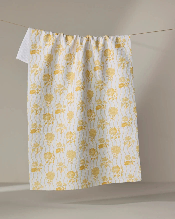 The Danelys Sidron "Spring Wave" tea towel, ultra-absorbent and white with yellow floral and skull patterns, hangs on a clothesline against a neutral background.