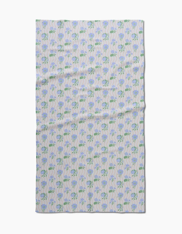 The Spring Wave blanket by Danelys Sidron features a symmetrical blue and green floral pattern on a pale background, made from post-consumer recycled materials.