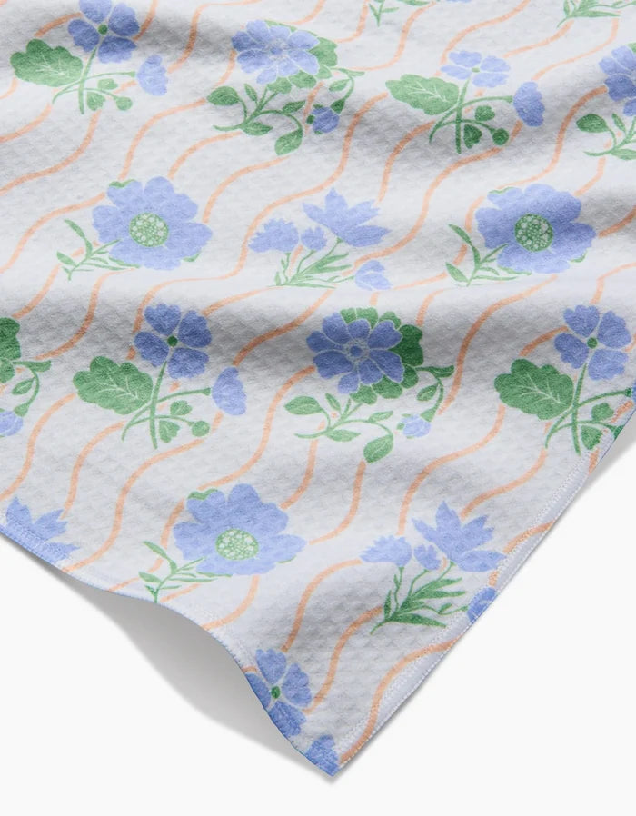 A close-up of Danelys Sidron’s Spring Wave, featuring ultra-absorbent textured fabric with wavy peach lines and clusters of blue flowers with green leaves on a white background.