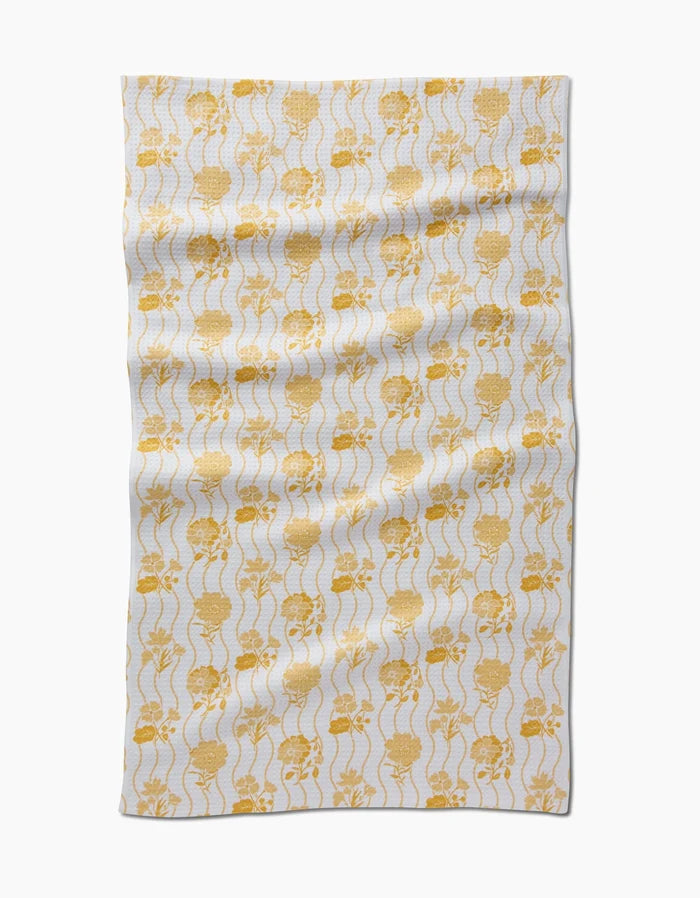 The Spring Wave tea towel by Danelys Sidron features yellow skulls and wavy vertical lines on soft Geoweave fabric. Its rectangular, white design is shown slightly wrinkled against a plain white background.