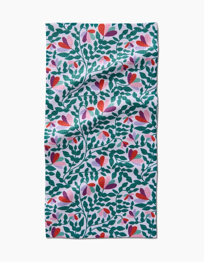 Spring Wavy Leaves by Claire Iglesias is a rectangular bar towel made from recycled materials, featuring a vibrant pattern of green leafy branches, heart-shaped red and pink flowers, and purple accents on white fabric.