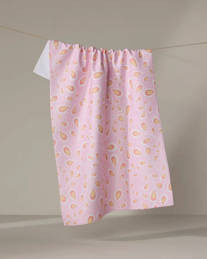 The Blissful Flamingo Springtime Wonders tea towel, made from recycled materials with pink fabric and scattered light red, orange, and yellow teardrop shapes, hangs on a clothesline against a neutral background.