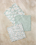 Three "Springtime" fabric napkins by Aubrey Fairchild sit on a beige surface: two display white daisies on light green, while the center napkin has a delicate white leaf pattern, all crafted from recycled kitchen towels.