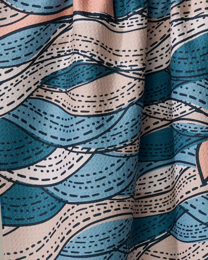 Close-up of Twig + Spark’s Squall kitchen towel, showing Geoweave fabric with a wavy blue, beige, and teal pattern. Dashed and solid lines evoke waves or leaves on the textured, softly draped recycled material.