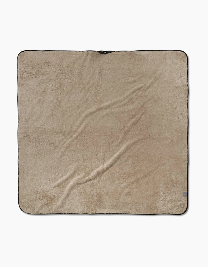 The Geometry Bark blanket is a large, square, beige fleece made from recycled materials with a slightly wrinkled texture and black trim, shown laid flat on a white background.