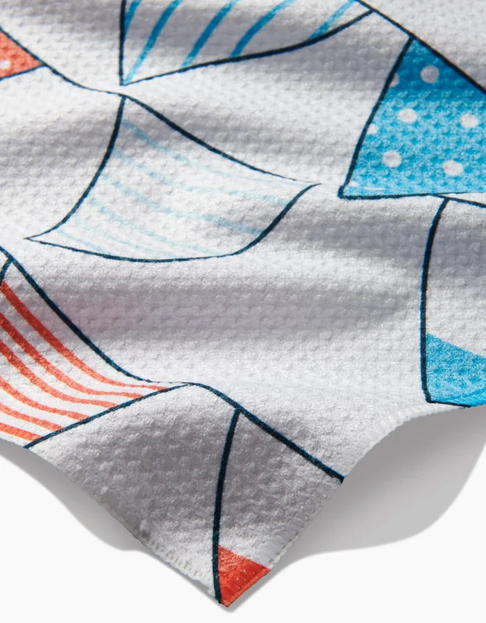 Close-up of the Sara Mari Stars Stripes And Dots Bar Towel, made from post-consumer recycled Geoweave™ fabric, featuring a textured waffle weave and geometric blue, red, and aqua shapes with stripes and polka dots.