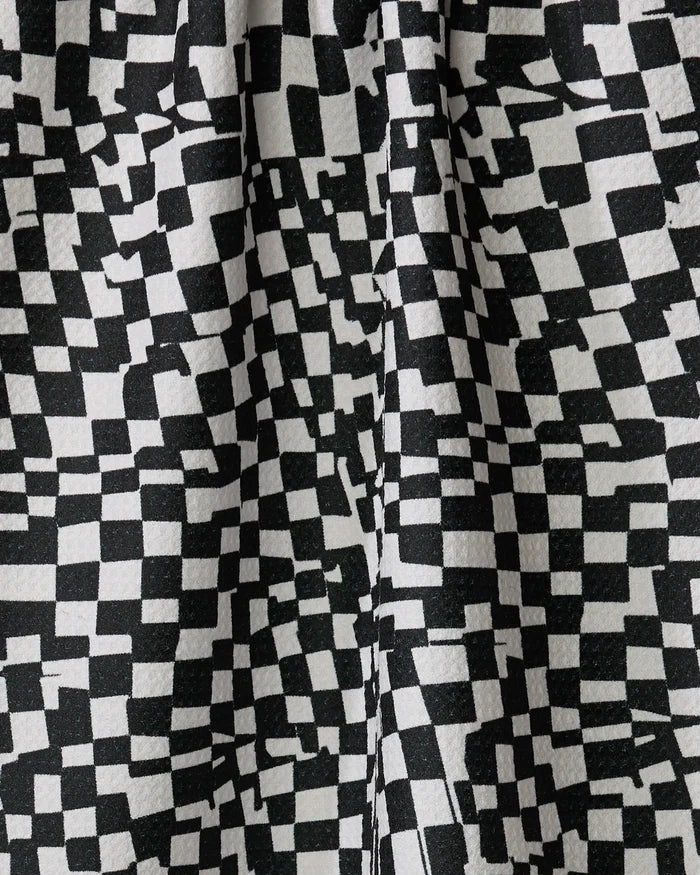 Close-up of the Geometry "Static" kitchen towel, showcasing its black and white irregular checkerboard pattern with uneven squares and textured folds—expertly crafted from recycled materials.