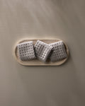 A wooden tray displays three neatly folded GEOMETRY Stone gray waffle washcloths, arranged in a row against a plain light beige background.