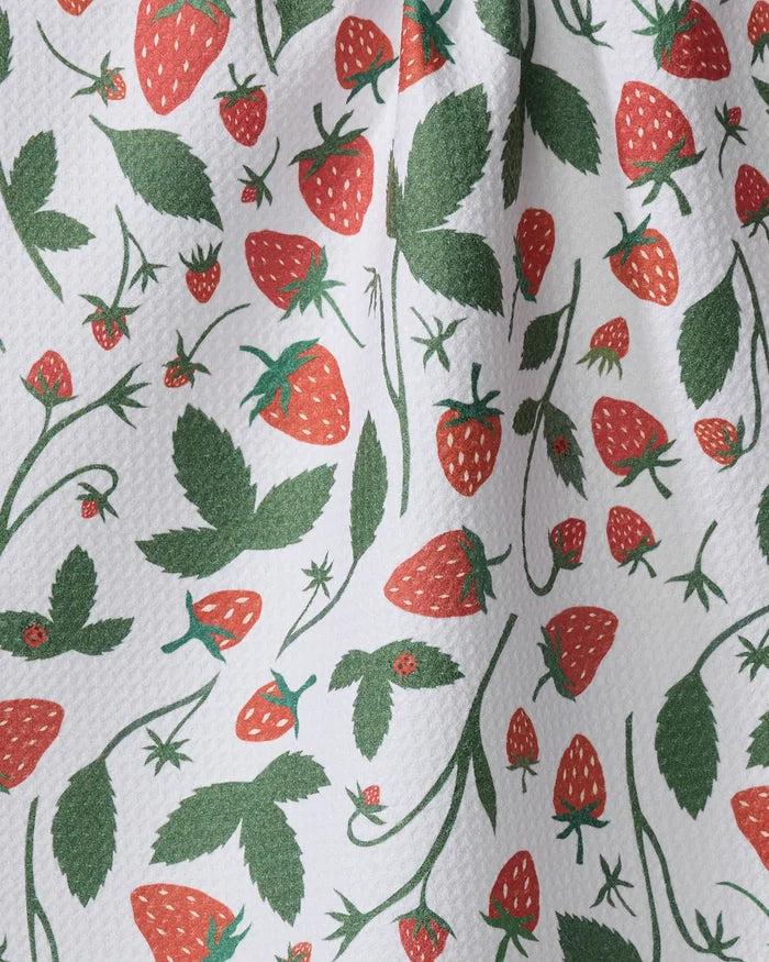 A close-up of Elana Gabrielle’s Strawberries recycled kitchen towel, featuring a printed pattern of red strawberries, green leaves, and small strawberry flowers on a white textured background.