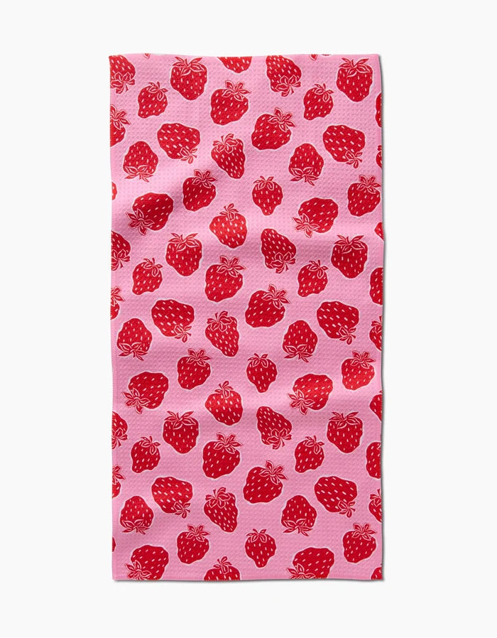 The Strawberry Fields Bar Towel by Charlie Rowan Designs, made from Geoweave fabric, features a pink background with a repeating red strawberry and green stem pattern, shown here against a white backdrop.