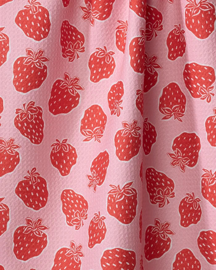 Close-up of Strawberry Fields tea towel by Charlie Rowan Designs, showing pink fabric with red strawberries and white seeds. The ultra-absorbent material has a slightly textured surface and soft draping folds.