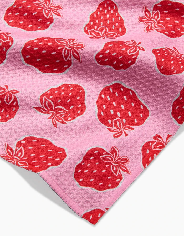Strawberry Fields by Charlie Rowan Designs: a pink Geoweave bar towel with large red strawberries, white seeds, and green leaves. Corner of the towel visible bottom right.