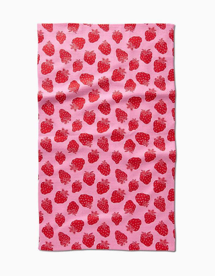 The Strawberry Fields tea towel by Charlie Rowan Designs, in pink and made from recycled materials, displays a repeating pattern of red strawberries with green leaves across its subtly textured surface.
