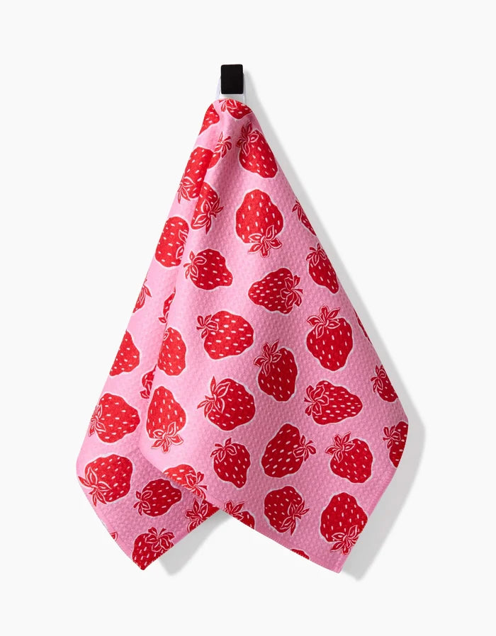 The Strawberry Fields Bar Towel by Charlie Rowan Designs features red strawberries and white dots on pink Geoweave fabric, hanging from a black loop against a white background.