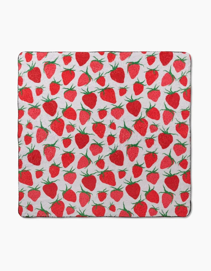 The Geometry Strawberry Sniff is a square blanket with a white background and a repeating red strawberry and green leaf pattern, made from recycled materials for eco-friendly comfort.