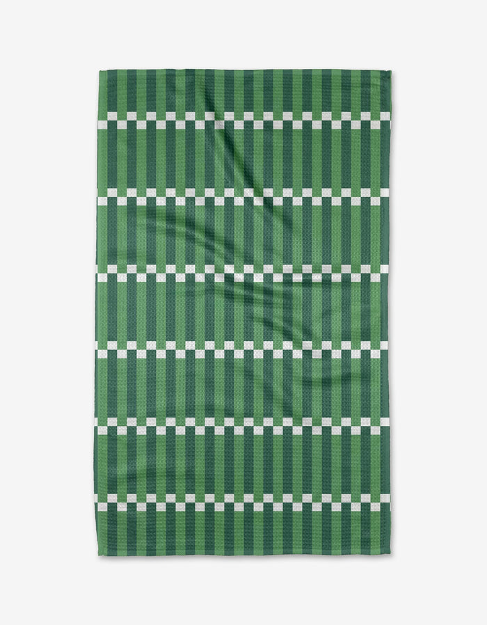 The Buy Guides Stripe Block - Greens is a rectangular tea towel in green, featuring horizontal white squares and dark green stripes on a lighter green background. Made from Geoweave fabric, it is shown flat with slight creases.