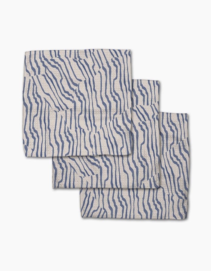 Three folded Stripe Funk Grounds napkins by Geometry, made from recycled materials, feature an abstract wavy blue line pattern and are stacked with slight overlap on a white background.