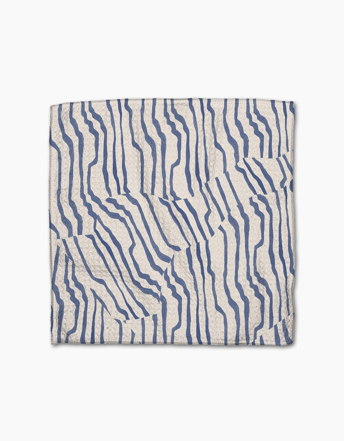 The Geometry Stripe Funk Grounds napkin features a folded white Geoweave fabric with an abstract blue wavy line pattern forming an irregular, striped design on a plain white background.