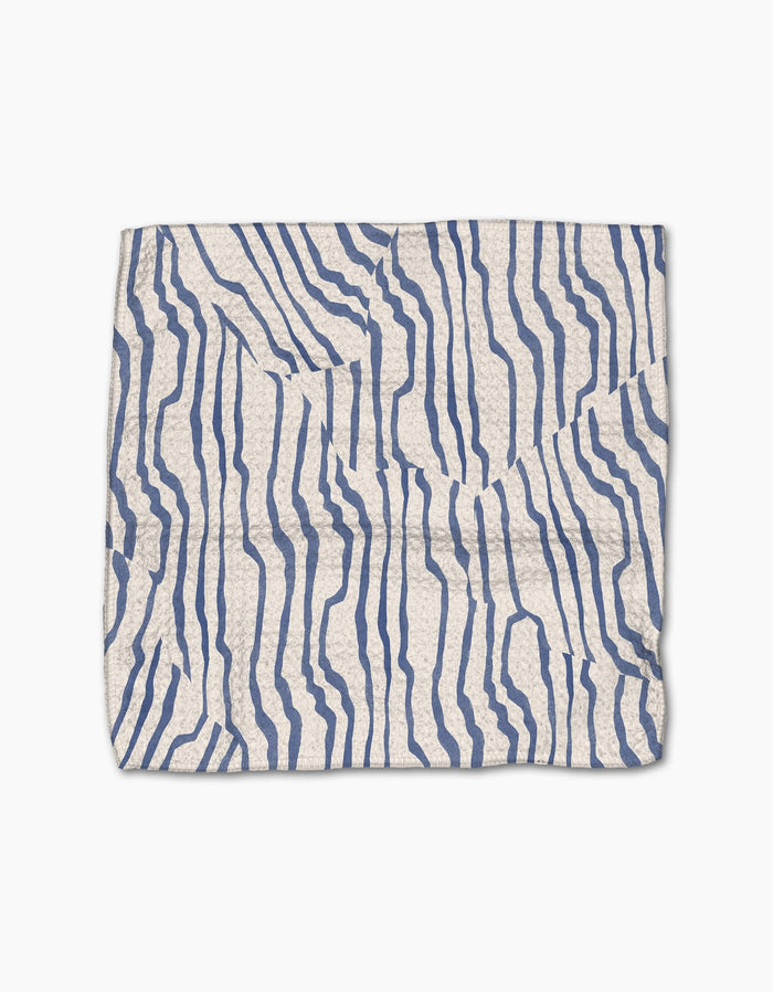 The Geometry Stripe Funk Grounds is a rectangular white dishcloth made from Geoweave fabric, featuring an abstract pattern of irregular wavy blue lines and visible creases on its surface.