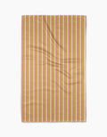 Stripe Mania by Geometry is a rectangular yellow tea towel with vertical red, pink, and white stripes, made from Geoweave™ fabric and shown flat with subtle folds on a white background.