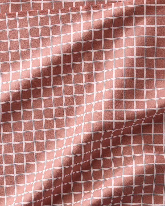 A Striped Harvest napkin by Charlie Rowan Designs in pink recycled fabric, featuring a white grid pattern with softly curved lines created by gentle folds and creases.
