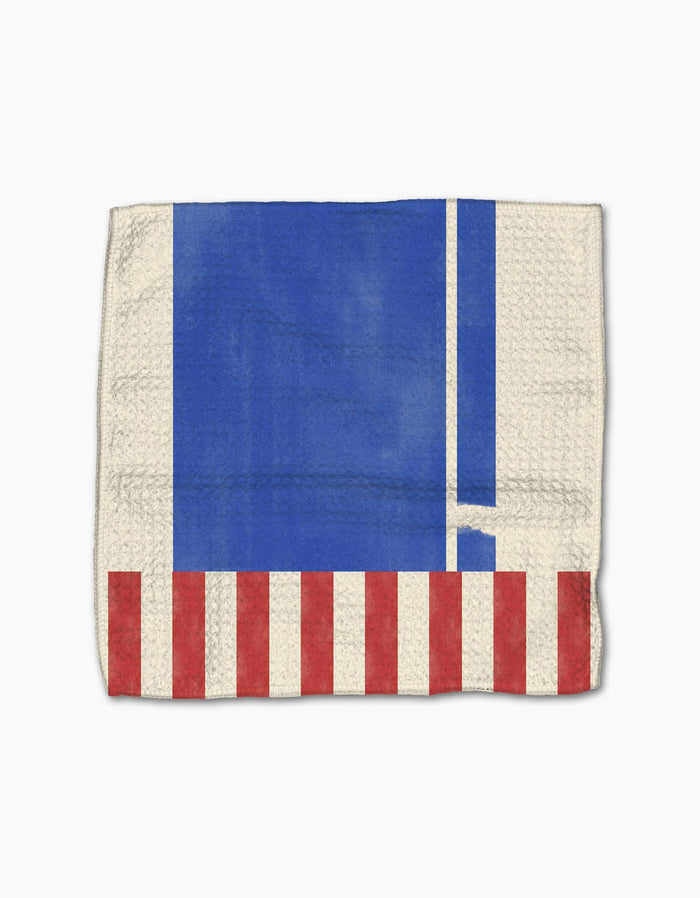 The Geometry Striped Heart dishcloth is made from recycled materials and features a blue rectangle, two white vertical stripes, and red and white stripes along the bottom edge on a beige background.