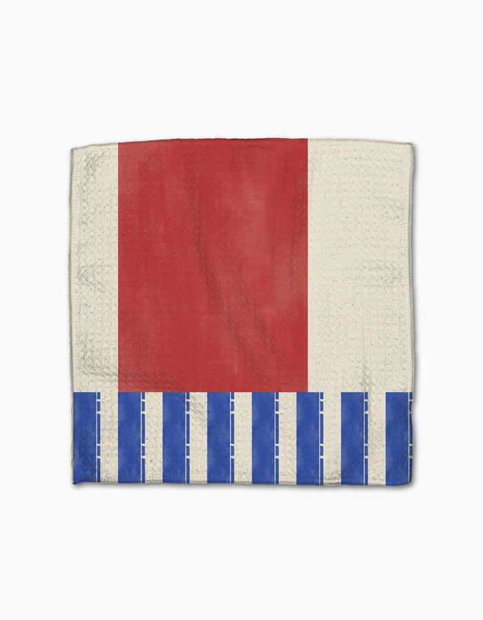 The Geometry Striped Heart is a rectangular dishcloth made from recycled materials, featuring a large red heart on an off-white background with vertical blue and white striped borders and a dashed pattern along the bottom edge.