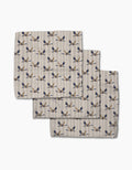 Three folded Striped Nautical Birds napkins by Geometry, featuring a blue and gold bird pattern on beige Geoweave fabric, are overlapped on a white background.