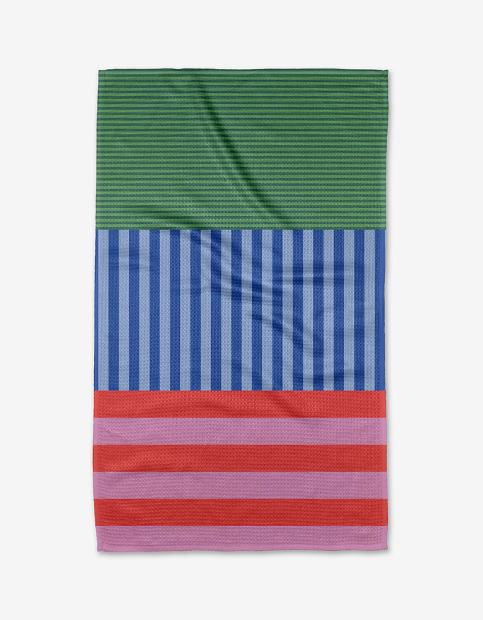 The Buy Guide’s Stripes on Stripes tea towel is crafted from ultra-absorbent Geoweave and features three bold sections: green with fine stripes, blue with vertical stripes, and red with pink horizontal stripes at the bottom.