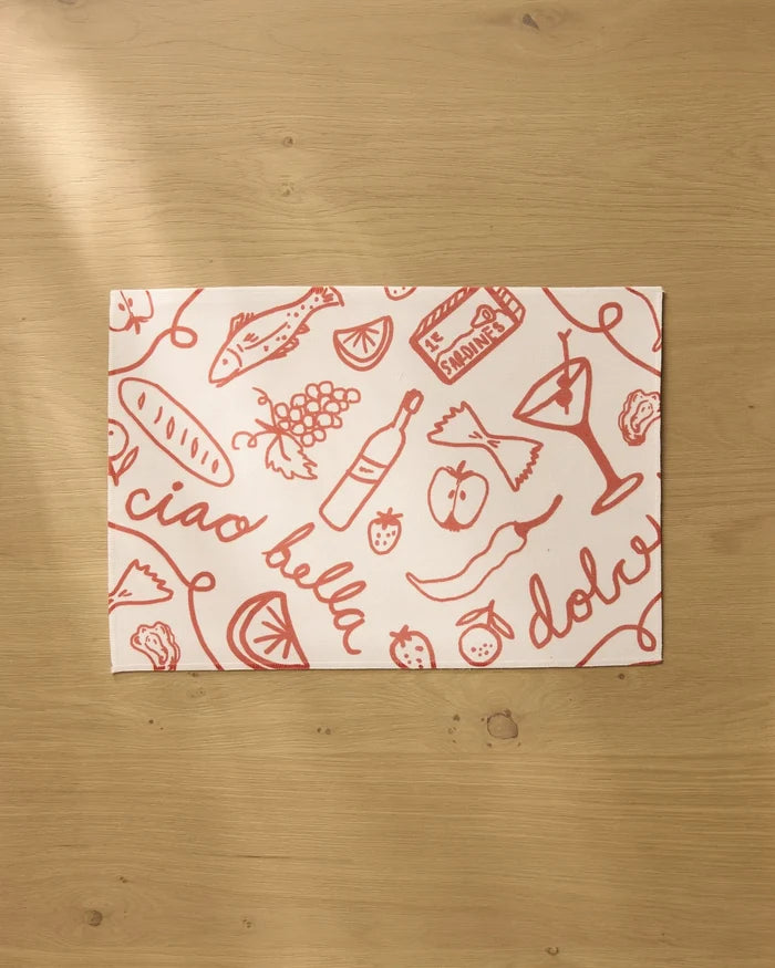The Summer Air placemat by Geometry features red Italian-themed sketches and phrases on white recycled fabric, resting on a light wooden surface. Both stylish and practical, these placemats are machine washable.