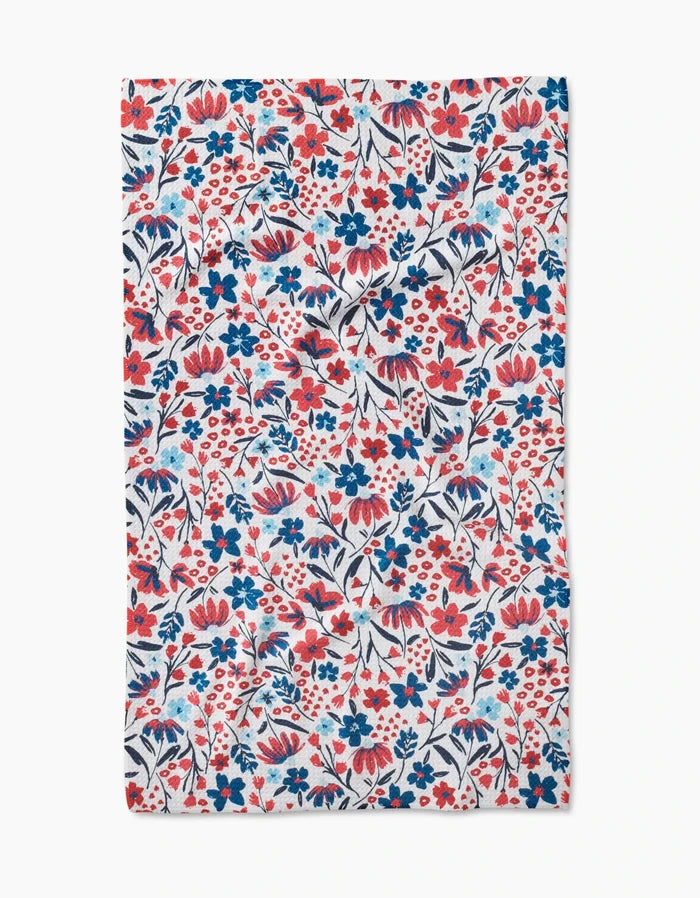 The Summer Bloom tea towel by Hufton Studio is made from Geoweave fabric and features a lively, dense floral pattern with red, blue, and navy flowers and leaves on a white background.