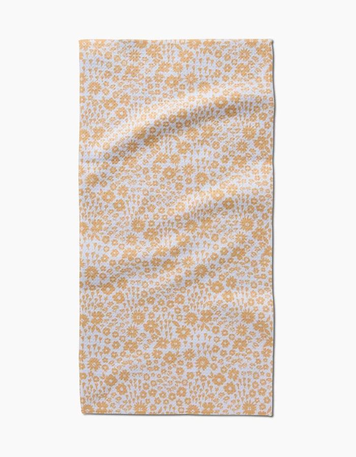 The Summer Fields bar towel by Hufton Studio features a white background with a repeating yellow floral pattern. Made from ultra-absorbent recycled materials, it’s shown laid flat with gentle creases.