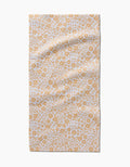 The Summer Fields bar towel by Hufton Studio features a white background with a repeating yellow floral pattern. Made from ultra-absorbent recycled materials, it’s shown laid flat with gentle creases.