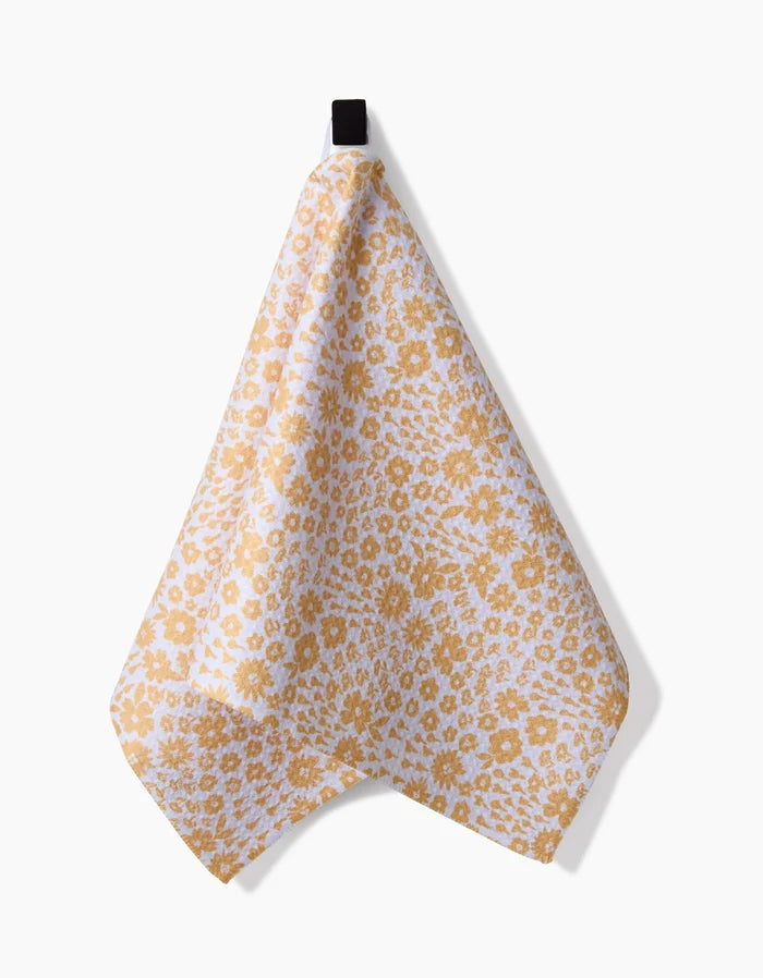 The Summer Fields bar towel by Hufton Studio, featuring a yellow floral pattern on white and made from recycled materials, hangs from a black loop against a plain white background.