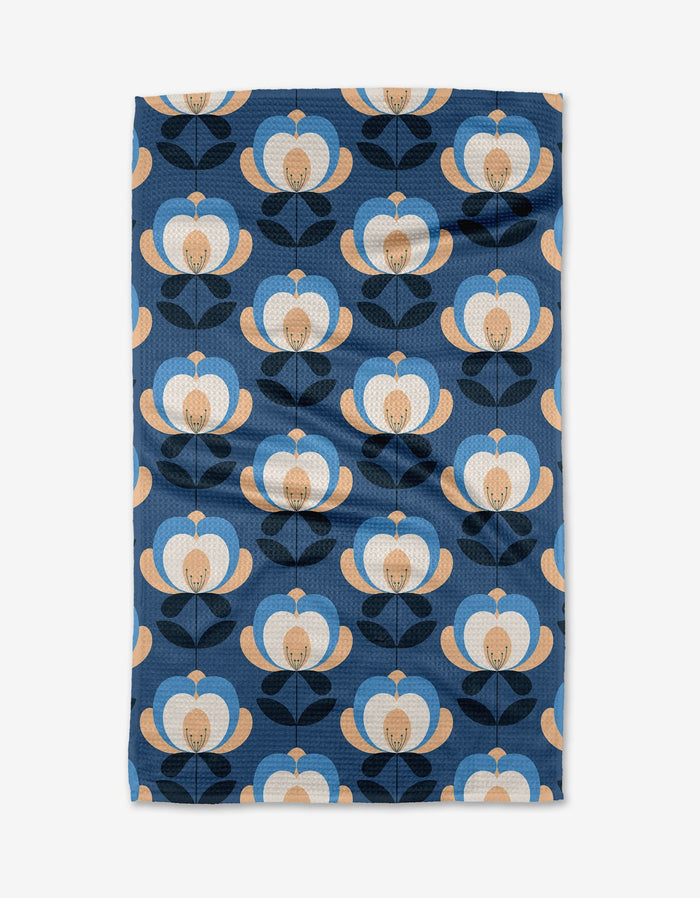 The Summer Florals tea towel by Blissful Flamingo is made from Geoweave fabric and showcases a retro floral pattern in blue, beige, and black on a dark blue background, with rounded petals and stylized leaves in neat rows.