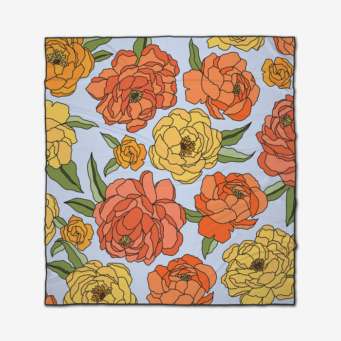 The GEOMETRY Summer Flowers Micro-loop Beach Blanket is square-shaped, displaying large yellow, orange, and red flowers with green leaves on a light blue background.