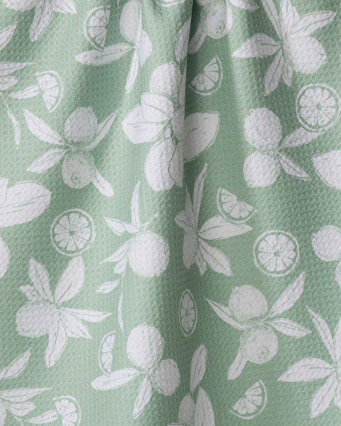 The Summer Limes tea towel by Hufton Studio features a green textured fabric with white lime and leaf patterns, made from recycled materials and designed to be quick-drying for everyday use.