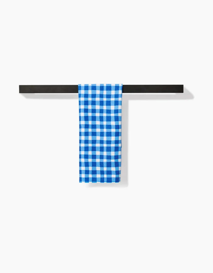 A Summer Plaid towel by Danelys Sidron, featuring blue and white checks in Geoweave fabric, hangs neatly over a black horizontal bar against a plain white background.