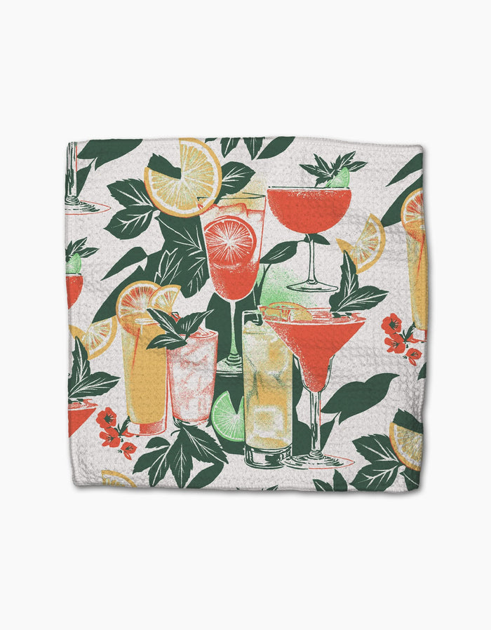 The Geometry Summer Refreshments dishcloth displays cocktail glasses with vibrant drinks, lemon slices, orange wedges, green leaves, and red flowers on a white background.