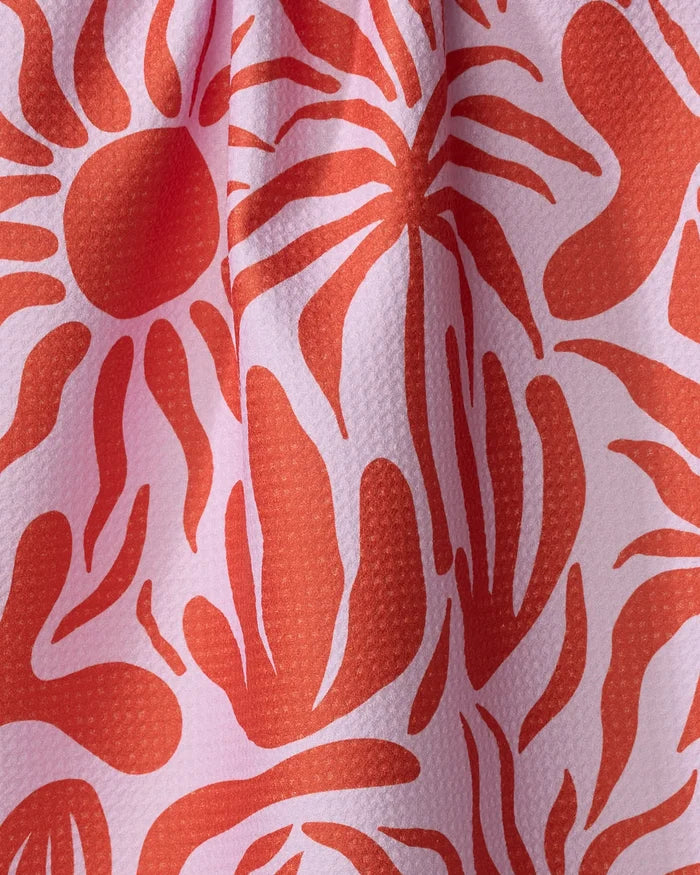 A close-up of the “Summer Sunset” dish towel by Marina Solodka reveals pink textured fabric with abstract red sunburst and flowing patterns. The absorbent material is softly gathered, creating gentle folds and shadows.